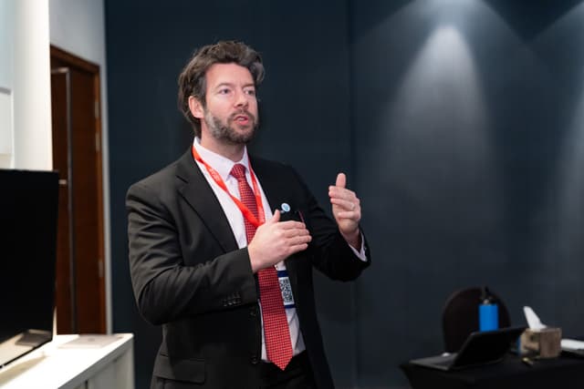 Alex presenting and gesturing during a conference talk